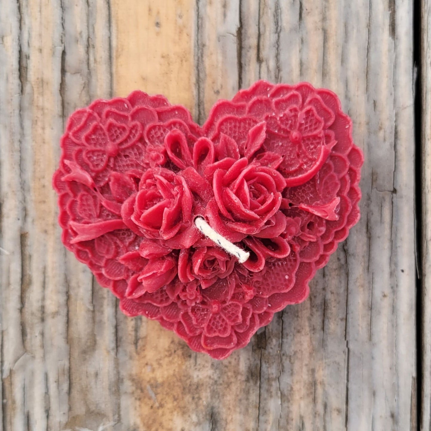 A handmade heart-shaped candle with roses in dark red.