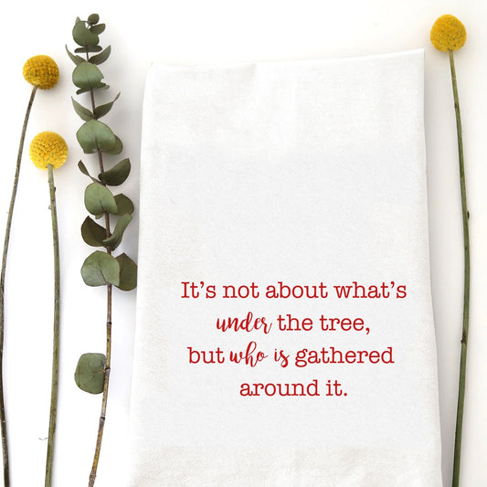 A holiday tea towel with the saying "It's not about what's under the tree, but who is gathered around it" printed on it.