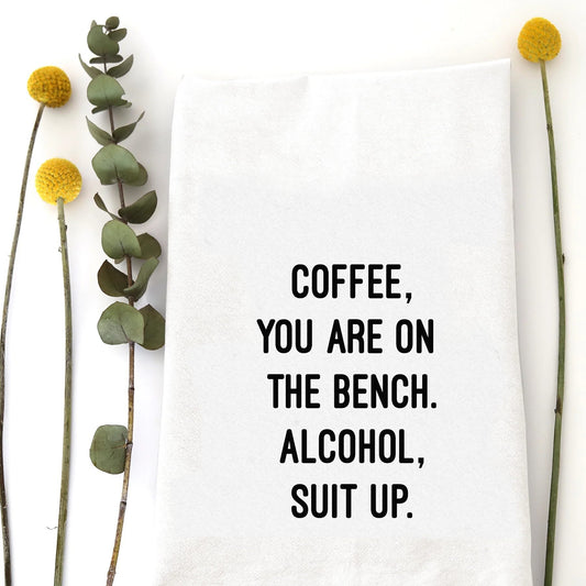 A tea towel with a funny saying - Coffee, you are one the bench. Alcohol, suit up.