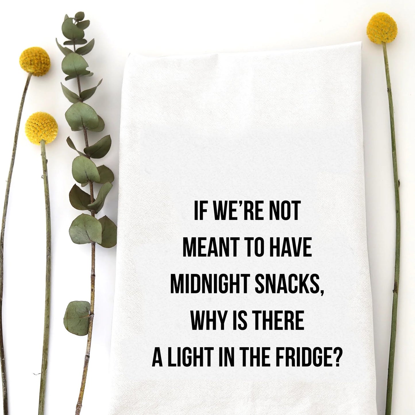 A tea towel with a funny saying - If we're not meant to have midnight snacks, why is there a light in the fridge?